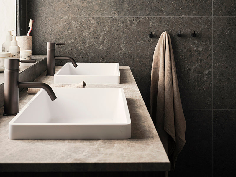 Kaksi valkoista pesuallasta ja kaksi hanaa. Takaseinällä neljä pyyhekoukkua, jossa yhdessä roikkuu pyyhe. 